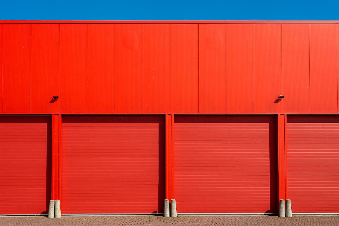 Bright red industrial garage doors in a modern building facade under a clear blue sky.
