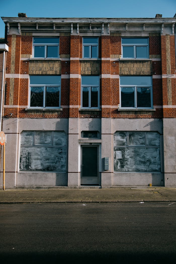 Front view of an abandoned building with a brick exterior and multiple windows.